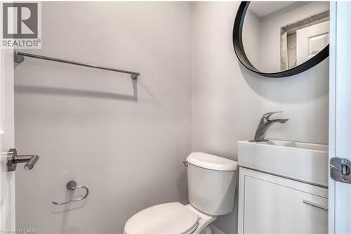 White vanity with integrated sink, chrome faucet, and circular black-framed mirror - 23 Gibson Avenue, Hamilton, ON 