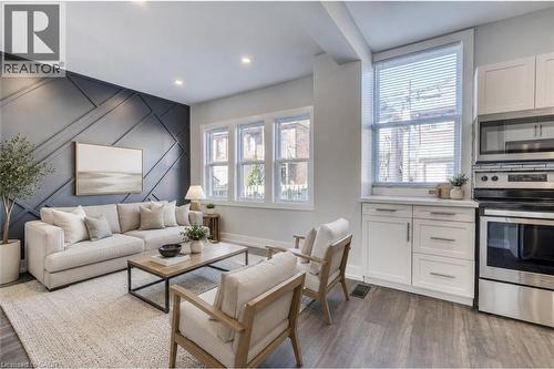 Accent wall with geometric paneling, recessed lighting, wood-finish flooring, white kitchen cabinetry, and stainless steel appliances - 23 Gibson Avenue, Hamilton, ON 