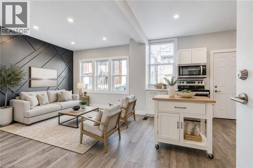Open-concept living space featuring wood-finish flooring, recessed lighting, and a geometric accent wall - 23 Gibson Avenue, Hamilton, ON 