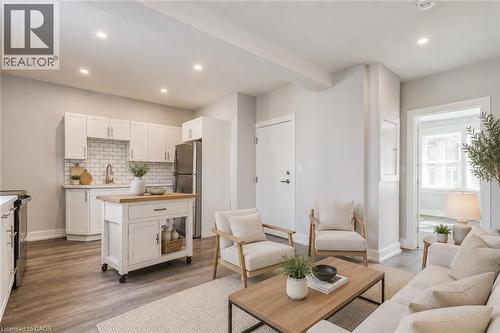 Open concept living area featuring wood-finish flooring, recessed lighting, and a kitchen with white cabinetry and a subway tile backsplash - 23 Gibson Avenue, Hamilton, ON 