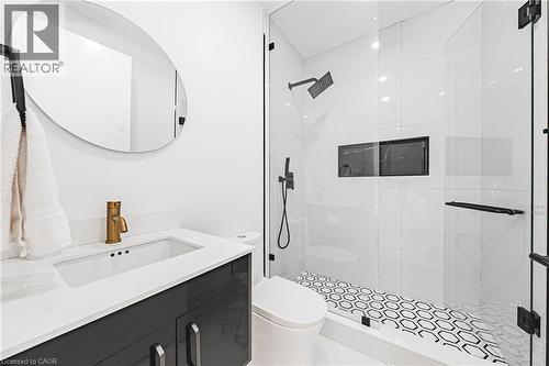 Modern bathroom featuring a glass-enclosed shower with black hexagonal floor tiling, a sleek vanity with a rectangular sink, and a gold-tone faucet - 4511 Guelph Line, Burlington, ON 