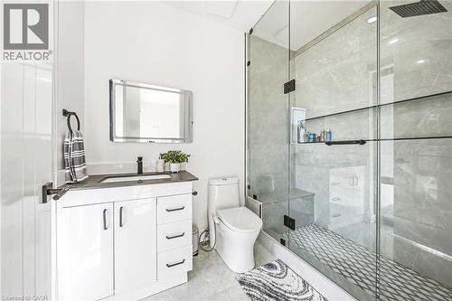 White vanity with dark countertop, frameless glass shower enclosure, large format wall tile, mosaic shower floor, and matte black fixtures - 4511 Guelph Line, Burlington, ON 