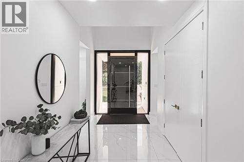 Bright entryway featuring large format tile flooring, a modern glass entry door, recessed lighting, and a white interior door with a gold-tone handle - 4511 Guelph Line, Burlington, ON 
