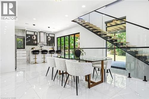 Open-concept interior featuring large format tile flooring, a modern kitchen with a waterfall island, a glass-paneled staircase, and expansive glass doors - 4511 Guelph Line, Burlington, ON 
