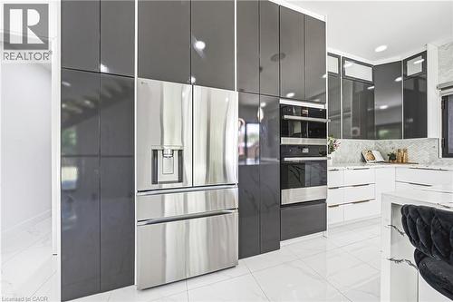 Contemporary kitchen featuring high-gloss gray cabinetry, stainless steel multi-door refrigerator with ice and water dispensers, white quartz countertops, integrated wall-mounted oven and microwave co - 4511 Guelph Line, Burlington, ON 