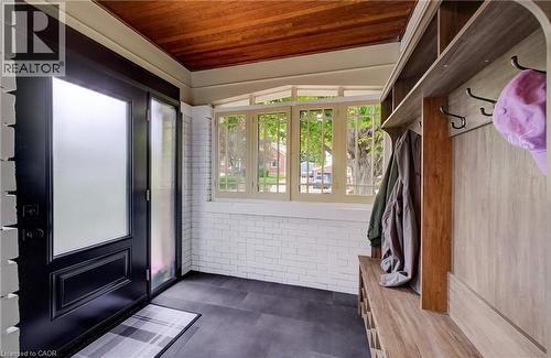 Entryway featuring a dark-finish door with frosted glass, built-in storage with hooks and shelving, light wood-finish ceiling, and white brick-finish walls - 90 Brock Street, Kitchener, ON 