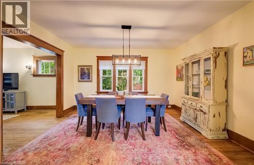 Warm dining area with wood-finish flooring, featuring a multi-light linear chandelier and a large window with wood trim - 90 Brock Street, Kitchener, ON 