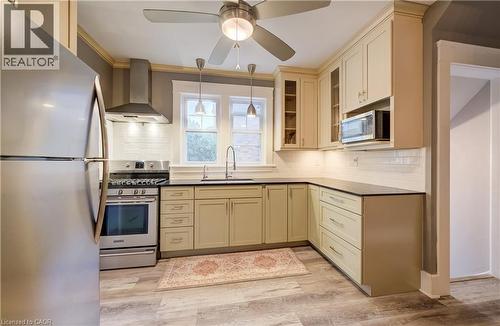 Kitchen featuring light-toned cabinetry, dark countertops, a subway tile backsplash, and wood-finish flooring - 90 Brock Street, Kitchener, ON 