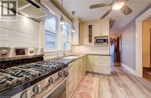 Stainless steel range with a coordinating range hood, white subway tile backsplash, wood-finish flooring, and cream-colored cabinetry with a built-in microwave - 90 Brock Street, Kitchener, ON 
