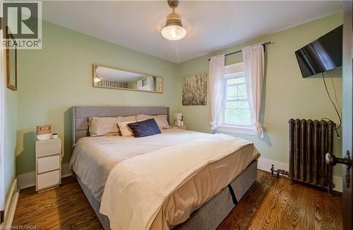 Hardwood flooring, painted walls, ceiling-mounted light fixture, window with trim, and a radiator - 90 Brock Street, Kitchener, ON 
