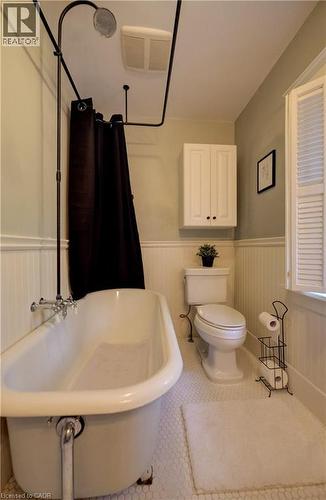 Clawfoot tub with wall-mounted shower fixture, white hexagonal tile flooring, wainscoting, and a wall-mounted storage cabinet - 90 Brock Street, Kitchener, ON 