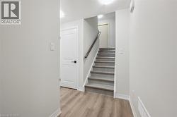 Wood-finish flooring, staircase with tile treads, white interior doors, and contemporary wall-mounted lighting - 