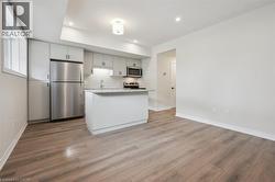 Kitchen island with a light-toned countertop, stainless steel appliances, wood-finish flooring, recessed lighting, and white cabinetry - 