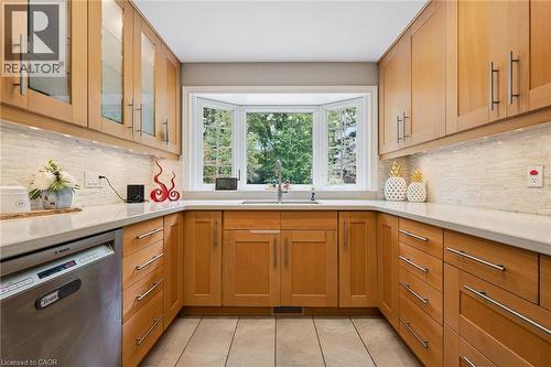 U-shaped kitchen featuring wood cabinetry, a bay window with a sink, stainless steel appliances, light-toned countertops, and tile flooring - 334 Coleridge Drive, Waterloo, ON 