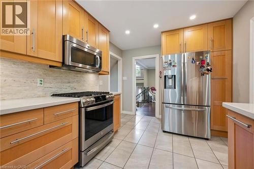 Light wood-finish cabinetry with stainless steel hardware, stainless steel appliances, light-toned backsplash, white countertops, and tiled flooring - 334 Coleridge Drive, Waterloo, ON 