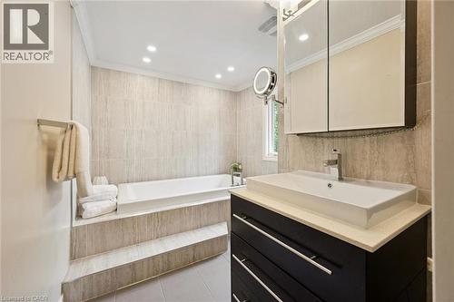 Recessed lighting, tiled walls, built-in bathtub, dark wood-finish vanity with drawer storage, and a rectangular vessel sink - 334 Coleridge Drive, Waterloo, ON 