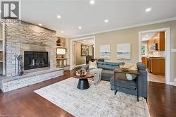 Stone-clad fireplace with a hearth, recessed lighting, wood-finish flooring, built-in shelving, and crown molding - 