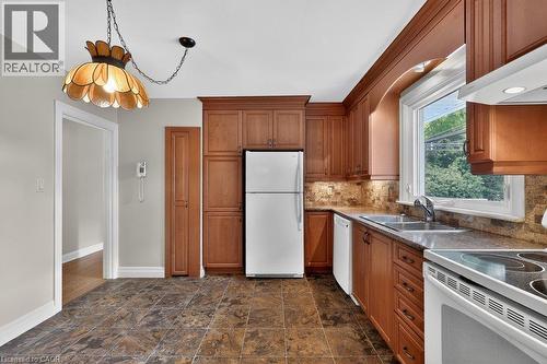 Kitchen featuring wood cabinetry, stone-look tile flooring, a tile backsplash, and a double basin sink - 948 Long Drive, Burlington, ON 