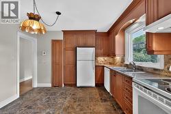 Kitchen featuring wood cabinetry, stone-look tile flooring, a tile backsplash, and a double basin sink - 