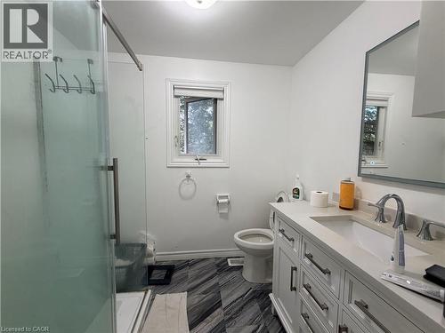 Glass-enclosed shower with a modern handle, white vanity with an integrated sink and chrome faucet, rectangular mirror with a framed edge, and dark patterned floor tiles - 450 Bridge Street W, Waterloo, ON 