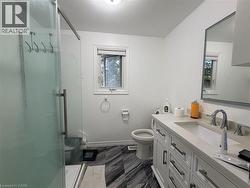 Glass-enclosed shower with a modern handle, white vanity with an integrated sink and chrome faucet, rectangular mirror with a framed edge, and dark patterned floor tiles - 