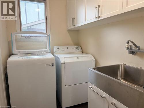 Utility area featuring white cabinetry, a stainless steel utility sink with a wall-mounted faucet, and wood-finish flooring - 450 Bridge Street W, Waterloo, ON 
