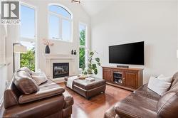 Vaulted ceiling with an arched window, a fireplace with a stone mantel, wood-finish flooring, and multiple tall windows - 