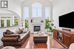 Vaulted ceilings with abundant natural light, a gas fireplace with a classic mantel, wood-finish flooring, and an arched entry - 