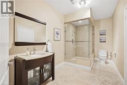 Spacious bathroom featuring a glass-enclosed shower, dark wood-finish vanity with an integrated sink, and light-toned tile flooring - 