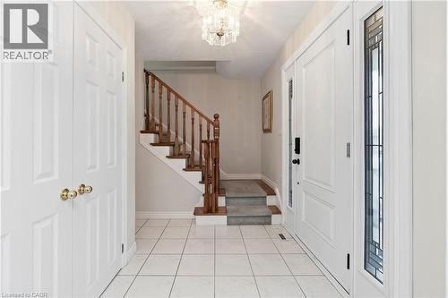 Entryway featuring white tile flooring, a staircase with wood banister and carpeted treads, a crystal chandelier, and a front door with a decorative glass sidelight - 36 Buckingham Drive, Hamilton, ON 