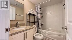 Bathroom featuring a vanity with an integrated sink, a light-toned countertop, a wall-mounted mirror, a toilet, and a bathtub with wave-patterned wall tiles - 