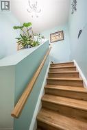 Stairway featuring wood-finish treads, a contrasting handrail, and a chandelier fixture - 
