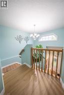 Wood-finish flooring, light blue wall paint, wood banister and railing, arched window, and chandelier - 