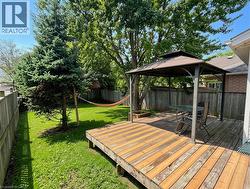 Expansive backyard featuring a wood deck, a metal-framed gazebo, mature trees, and a manicured lawn - 
