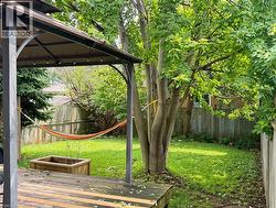 Spacious backyard featuring a wooden deck, metal gazebo structure, mature trees, and a wooden privacy fence - 