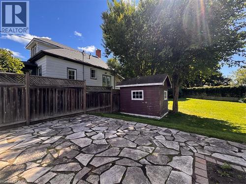 Expansive flagstone patio area with a privacy fence, complemented by a detached shed and a manicured lawn - 225 Bridgeport Road E, Waterloo, ON 