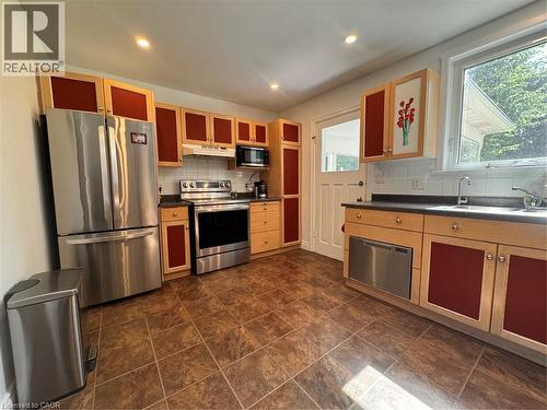 Kitchen featuring stainless steel appliances, wood-finish cabinetry with red panels, tiled flooring, and a white subway tile backsplash - 225 Bridgeport Road E, Waterloo, ON 
