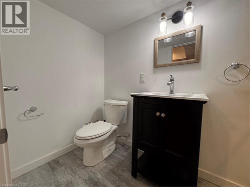 Bathroom featuring wood-finish flooring, a dark wood vanity with a white countertop, a framed mirror, and a two-light fixture - 225 Bridgeport Road E, Waterloo, ON 