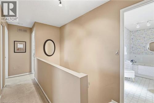 Hallway with carpet flooring and an open doorway to a bathroom featuring white floor and a built-in oval soaker tub - 89 Brigade Drive, Hamilton, ON 