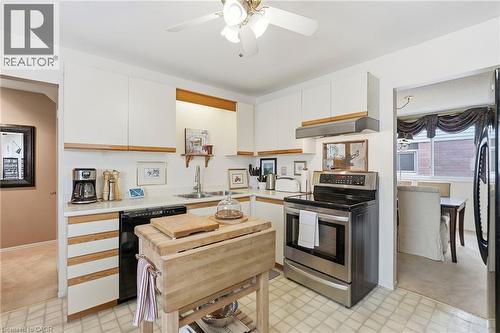 White cabinetry with integrated wood-tone accents, stainless steel range , and a built-in dishwasher - 89 Brigade Drive, Hamilton, ON 