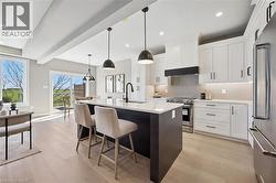 Kitchen featuring a dark island with white countertop, pendant lighting, stainless steel appliances, and wood-finish flooring - 