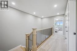 Carpeted hallway with recessed lighting, light wood railing with black spindles, and white paneled doors - 