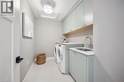 Compact laundry room featuring light green cabinetry, white countertops, a stainless steel sink with a gooseneck faucet, and a patterned backsplash - 