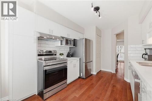 Kitchen featuring wood-finish flooring, white cabinetry, stainless steel appliances, and a tiled backsplash - 245 Bishop Street S Unit# 31, Cambridge, ON 
