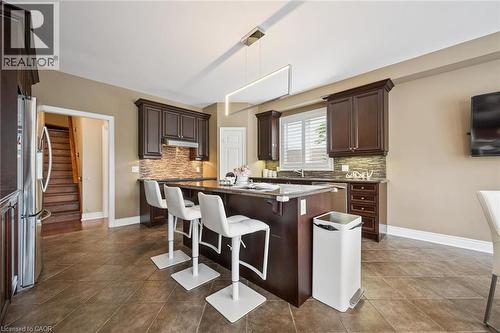 Kitchen featuring dark wood cabinetry, a central island with seating, stainless steel appliances, and tile flooring - 517 Topper Woods Crescent, Kitchener, ON 