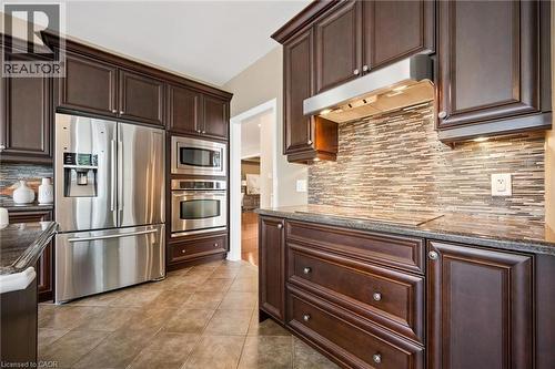 Dark wood-finish cabinetry with crown molding, stainless steel appliances, granite countertops, tile backsplash, and tile flooring - 517 Topper Woods Crescent, Kitchener, ON 