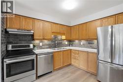 Stainless steel appliances, wood-finish cabinetry, subway tile backsplash, light wood-finish flooring, and under-cabinet lighting - 