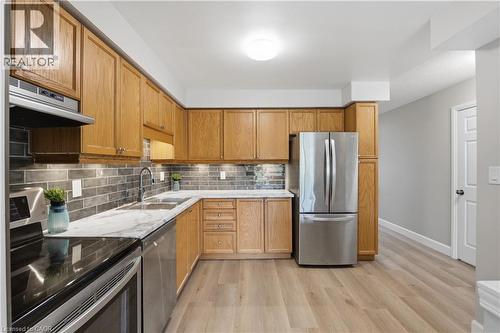 Kitchen featuring wood cabinetry, stainless steel appliances, a tile backsplash, and light-toned wood-finish flooring - 30 S Imperial Road Unit# 3, Guelph, ON 