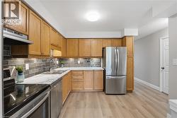 Kitchen featuring wood cabinetry, stainless steel appliances, a tile backsplash, and light-toned wood-finish flooring - 