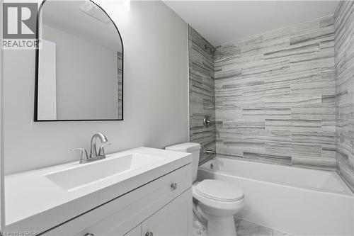 White vanity with integrated sink, brushed nickel faucet, arched mirror, and tiled shower surround with bathtub - 30 S Imperial Road Unit# 3, Guelph, ON 